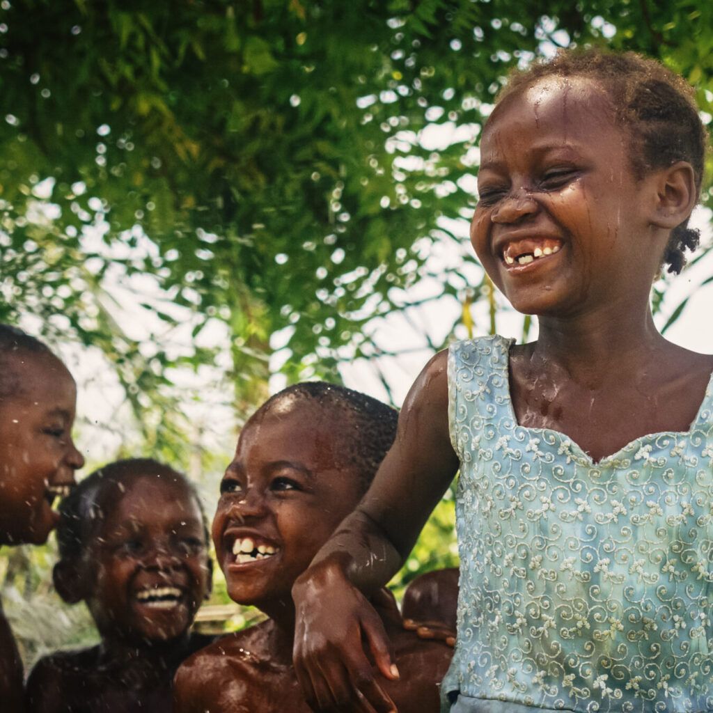 Five African school children jumping up and down in water spray with smiles on their faces