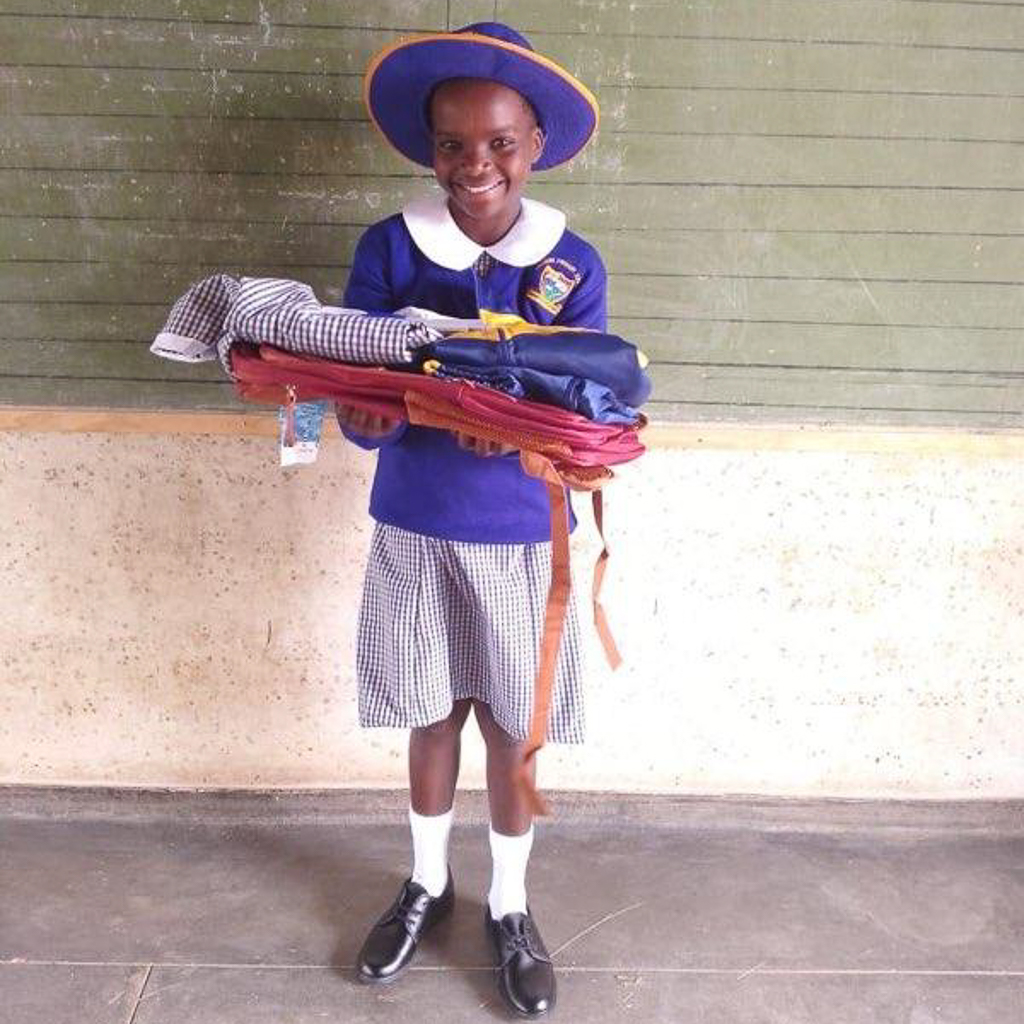 Child from Macheke smiling while holding school supplies and uniform